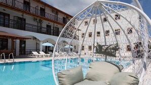 Zona de piscina con una hamaca colgante, sillas de descanso y sombrillas.