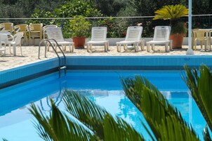 Una piscina con sillas de descanso blancas y plantas en macetas alrededor.