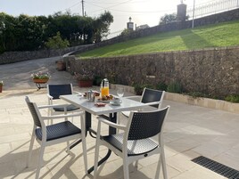 Un patio al aire libre con una mesa dispuesta para el desayuno, incluyendo croissants y jugo, rodeado de sillas.