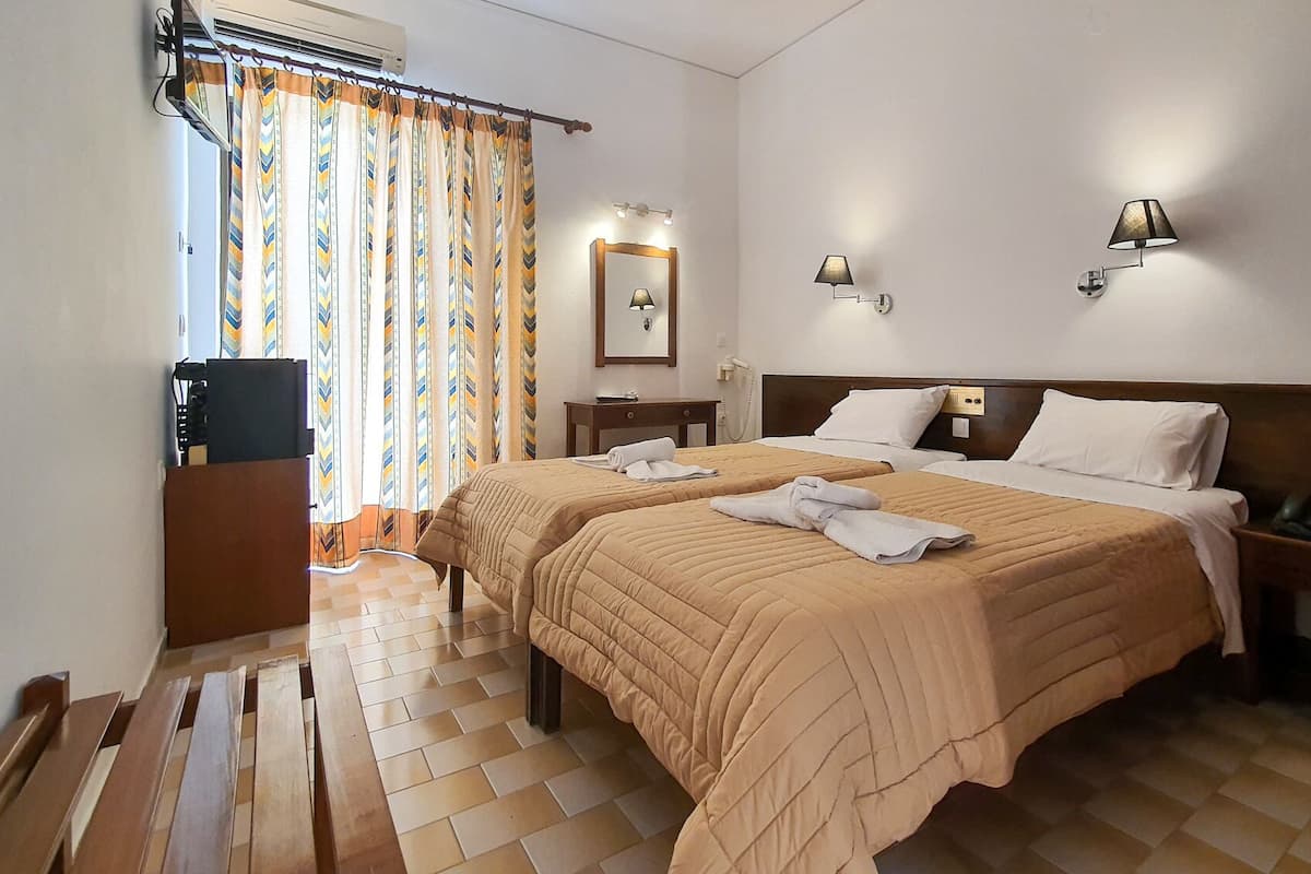A hotel room with two beds, a desk, a chair, a mirror, and a window with curtains.