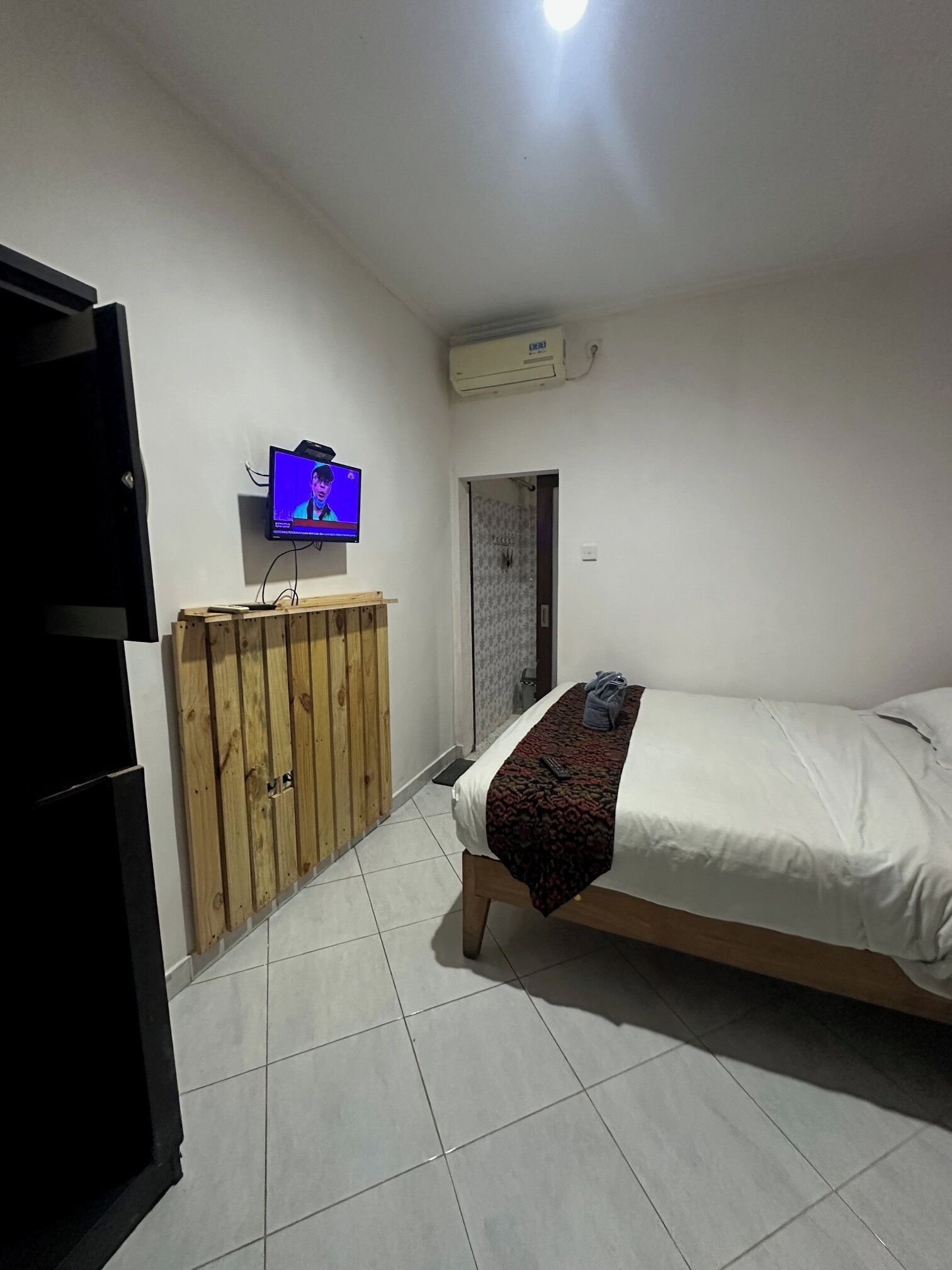 A bedroom with a bed, a wooden wardrobe, a television, and an air conditioning unit.