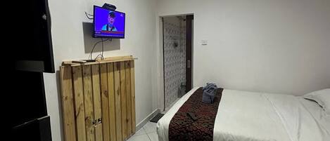 A bedroom with a bed, a wooden wardrobe, a television, and an air conditioning unit.