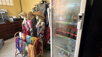 A room with a mannequin dressed in a traditional hat, a clothing rack with various garments, and a refrigerator stocked with beverages.