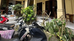 A courtyard with a yellow building, potted plants, and parked scooters. - Sari Buana Bed & Breakfast (Kuta)