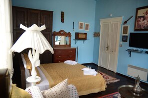 Een slaapkamer met een bed, een dressoir, een spiegel en een televisie aan de muur.