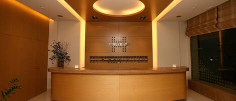 A hotel reception desk with a wooden finish, a glass display case, and a sign reading "HOTEL FLIVOS."