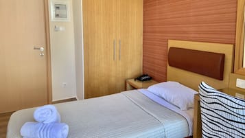 Ein Hotelzimmer mit einem Bett, einem Holzschrank, einem Nachttisch mit Telefon und einer Wandleuchte.