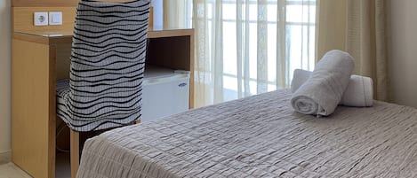 A hotel room with a bed, a desk with a chair, a television, and a window with curtains.