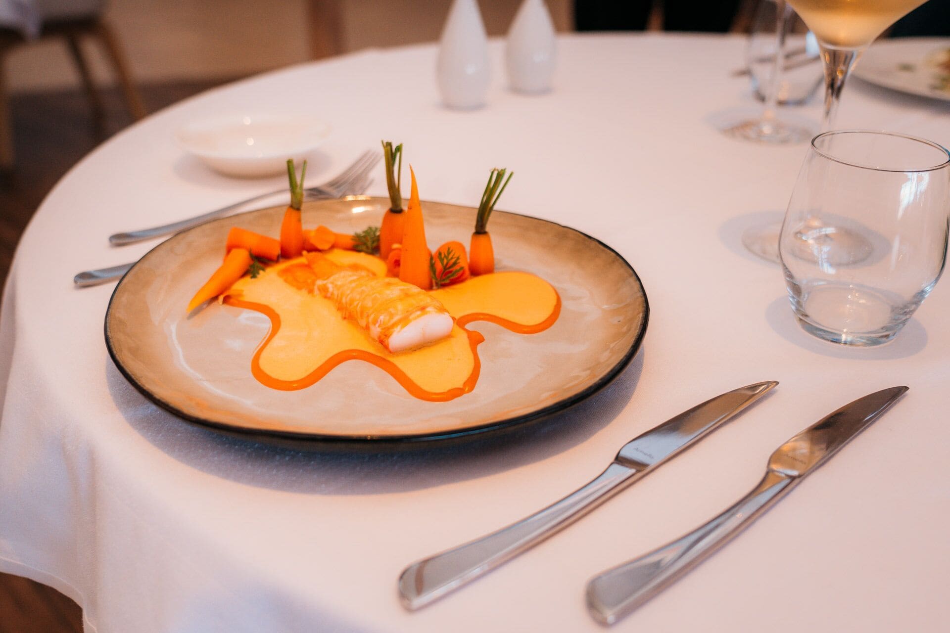 Een bord met een saus, wortels en kruiden op een witte tafel.