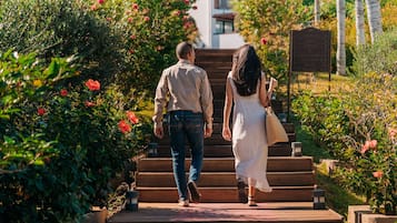 Una pareja camina por una escalera de madera rodeada de exuberante vegetación y plantas en flor.