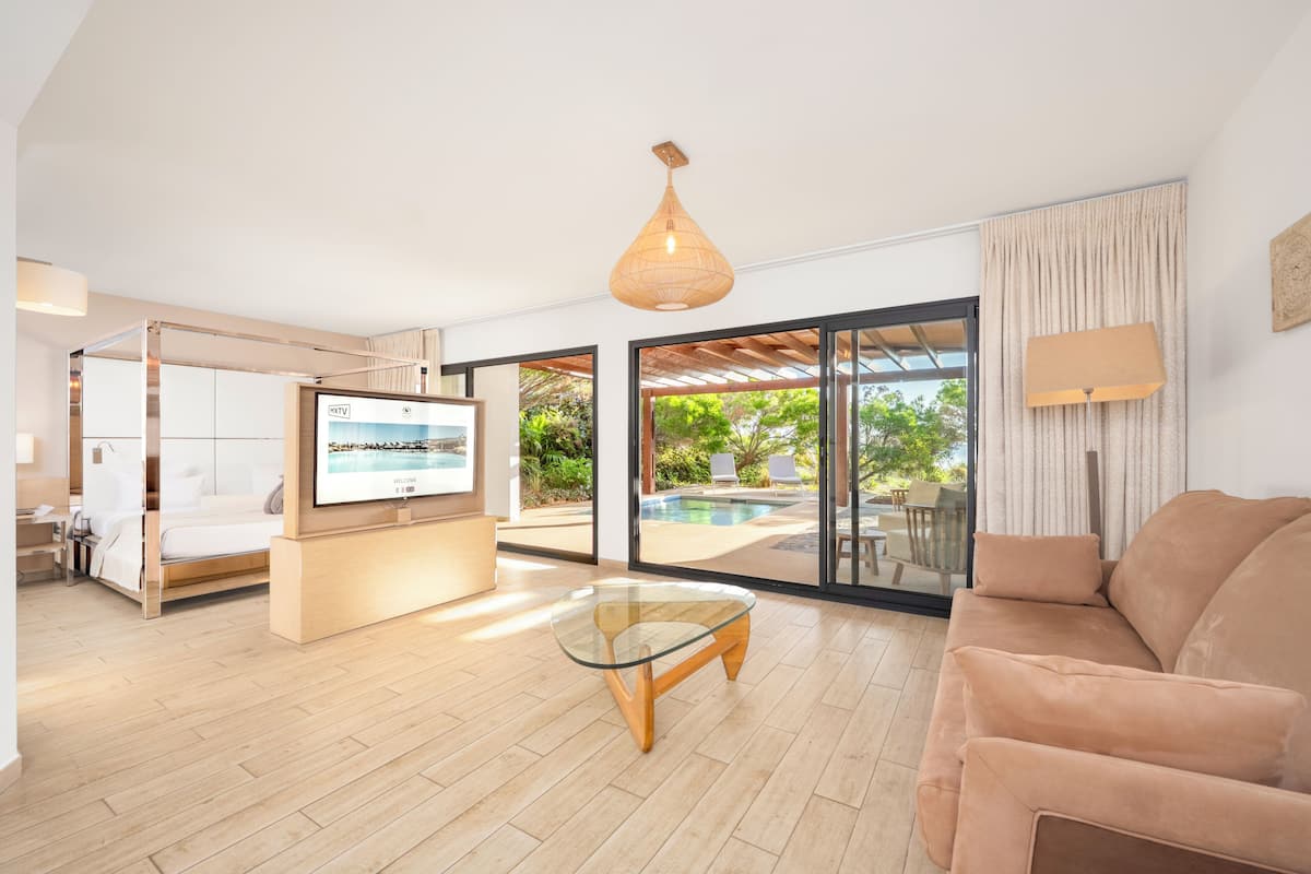 A modern living room with a glass coffee table, a sofa, a TV, and a pool view.