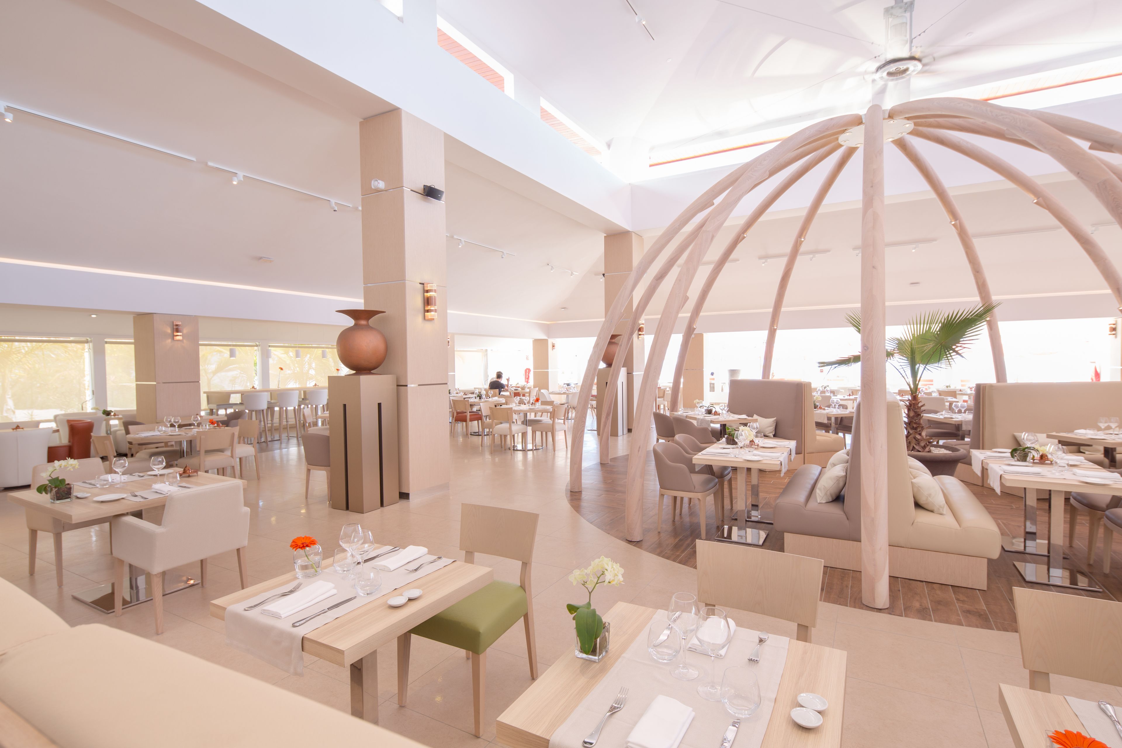A spacious, modern dining area with multiple seating arrangements, including tables and chairs, and a central decorative structure.