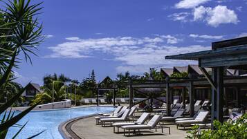 A poolside area with lounge chairs and umbrellas, surrounded by greenery and a clear blue sky.