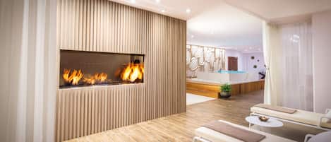 A modern spa room with a fireplace, lounge chairs, and a pool area.