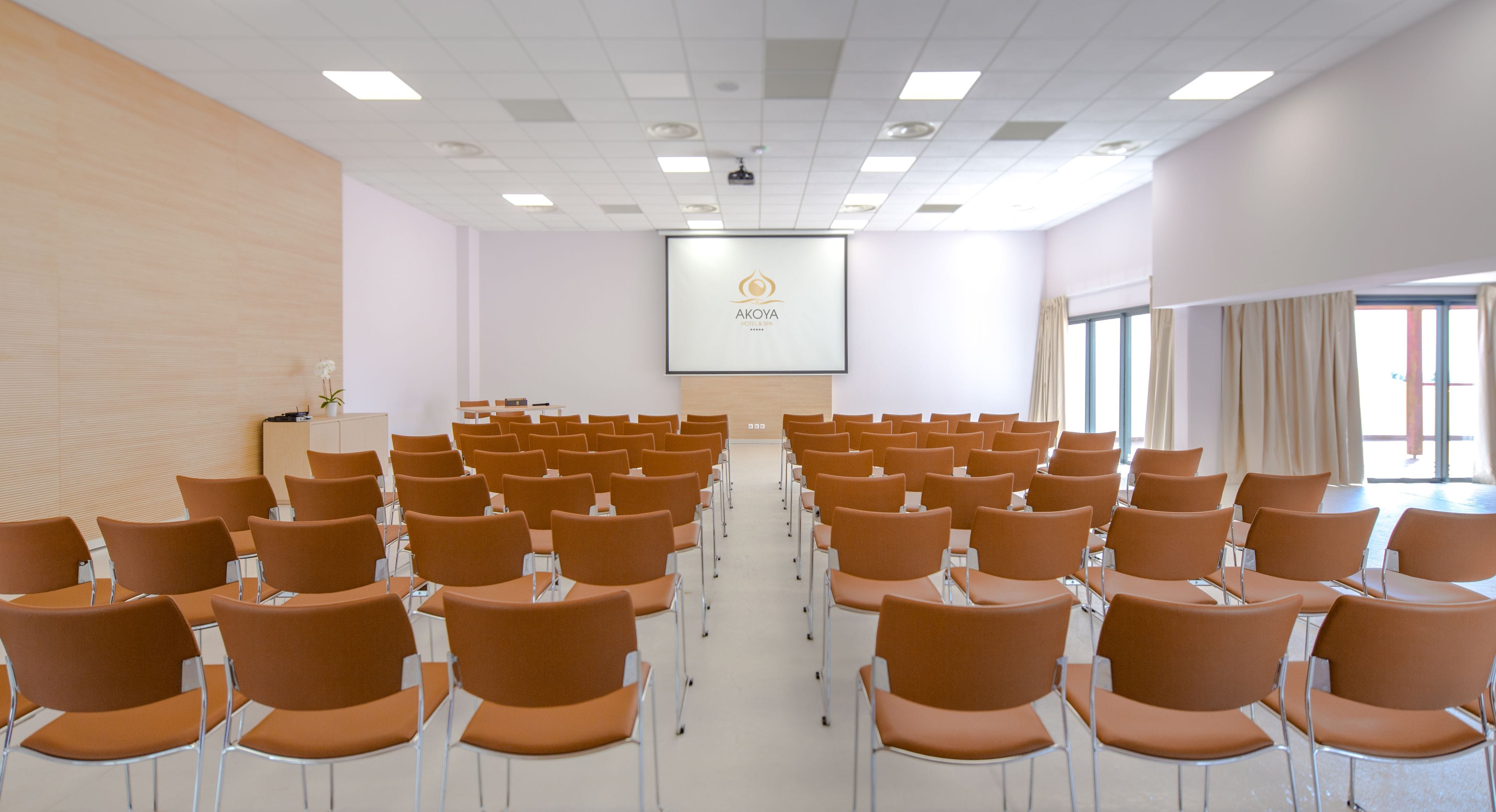 A conference room with rows of chairs, a projector screen, and a podium.