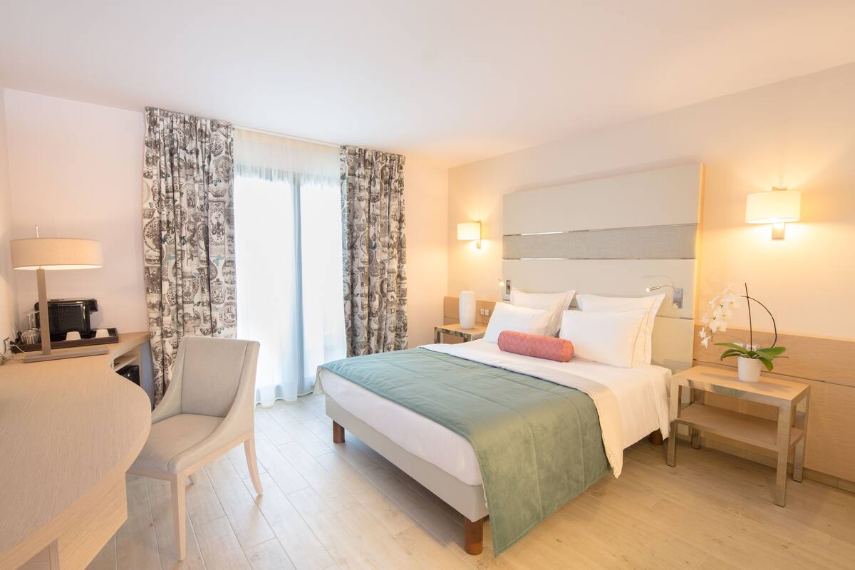 A modern hotel room with a bed, bedside tables, a desk, and a chair.