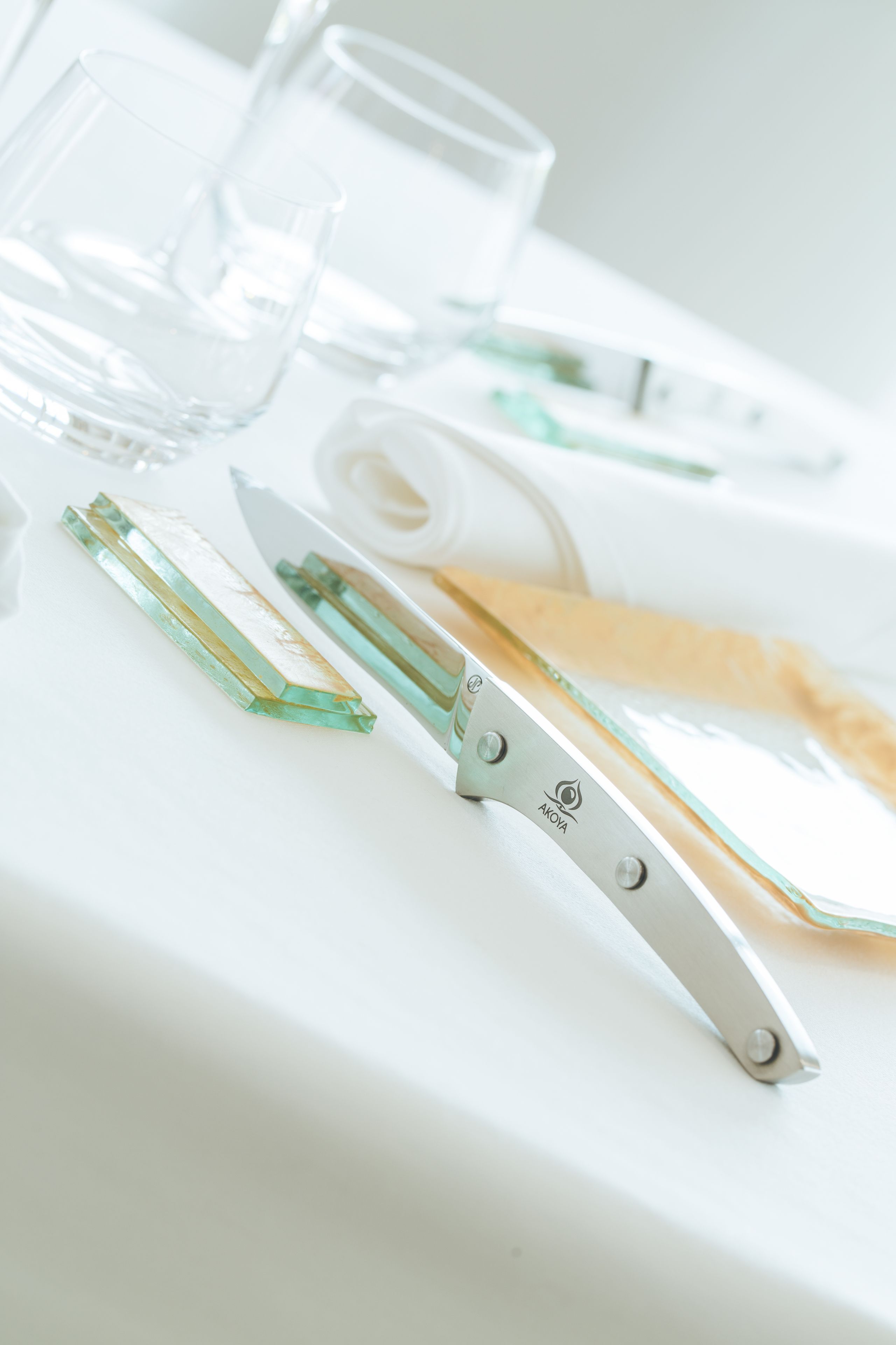 Une table recouverte d’une nappe blanche, avec des verres transparents, un couteau à manche vert et un rouleau d’essuie-tout.