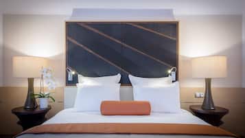 Quarto de hotel com uma cama grande, duas luminárias de cabeceira, uma mesa de cabeceira com uma planta e uma cabeceira decorativa.