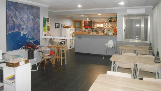 A dining area with tables and chairs, a kitchen area with a refrigerator, microwave, and shelves with bottles and glasses. - Hostal El Callejón (Tarragona)