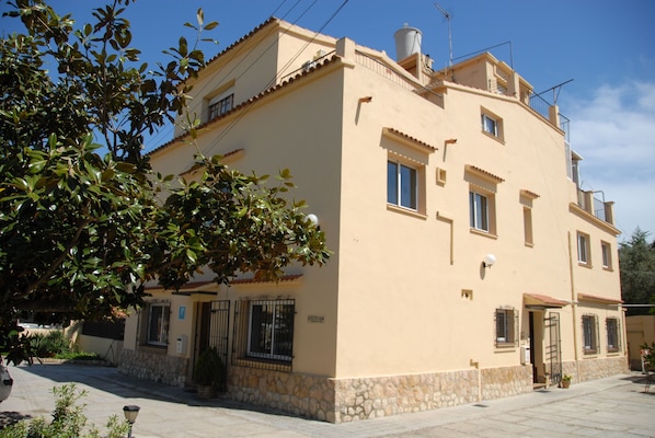 A two-story building with a stone base and a beige upper section. There are multiple windows, a visible door, and a small balcony.