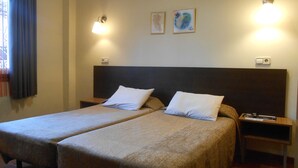 A double bed with two white pillows, a nightstand, a lamp, and two framed pictures on the wall. - Hostal El Callejón (Tarragona)