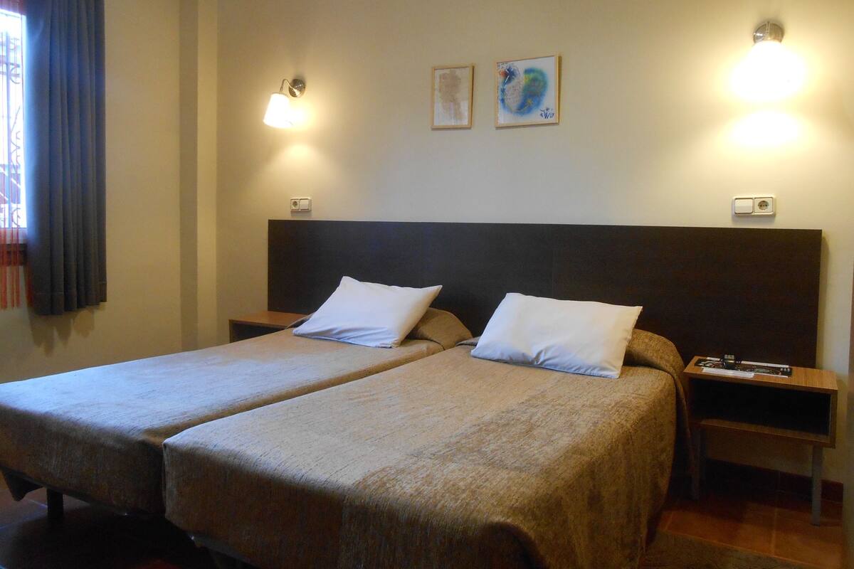 Un lit double avec deux oreillers blancs, une table de chevet, une lampe et deux tableaux encadrés au mur.