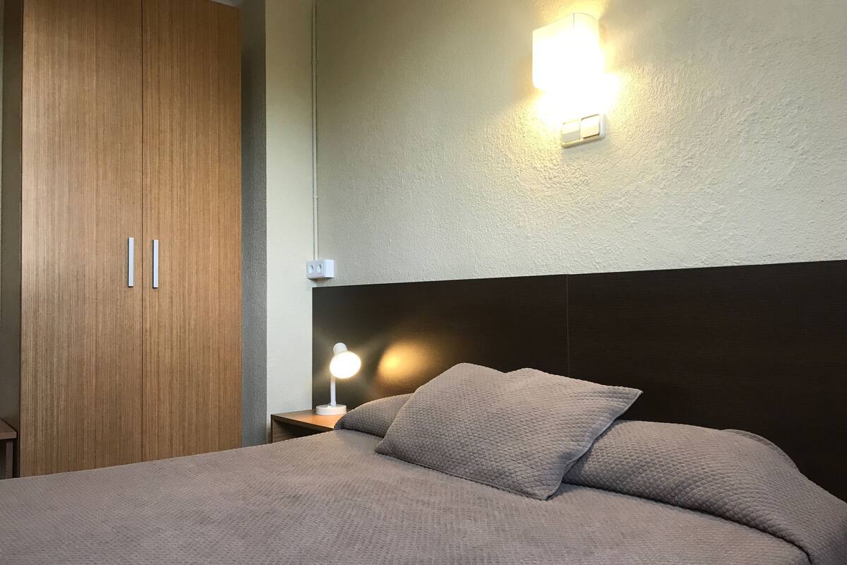 Une chambre à coucher comprenant un lit, une table de chevet, une lampe, un luminaire fixé au mur et une armoire.