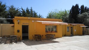 A yellow building with a reception area, outdoor seating, and a sign reading "RECEPCIÓ". - Hostal El Callejón (Tarragona)