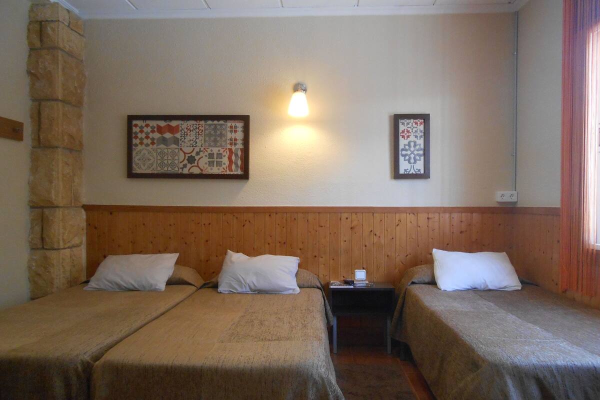 Une chambre avec deux lits simples, une tête de lit en bois, une table de chevet avec une lampe et deux tableaux encadrés au mur.