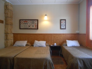 A room with two single beds, a wooden headboard, a nightstand with a lamp, and two framed pictures on the wall.