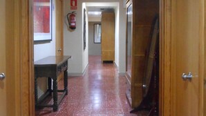 A hallway with red tiled flooring, wooden doors, and a fire extinguisher on the wall. - Hostal El Callejón (Tarragona)