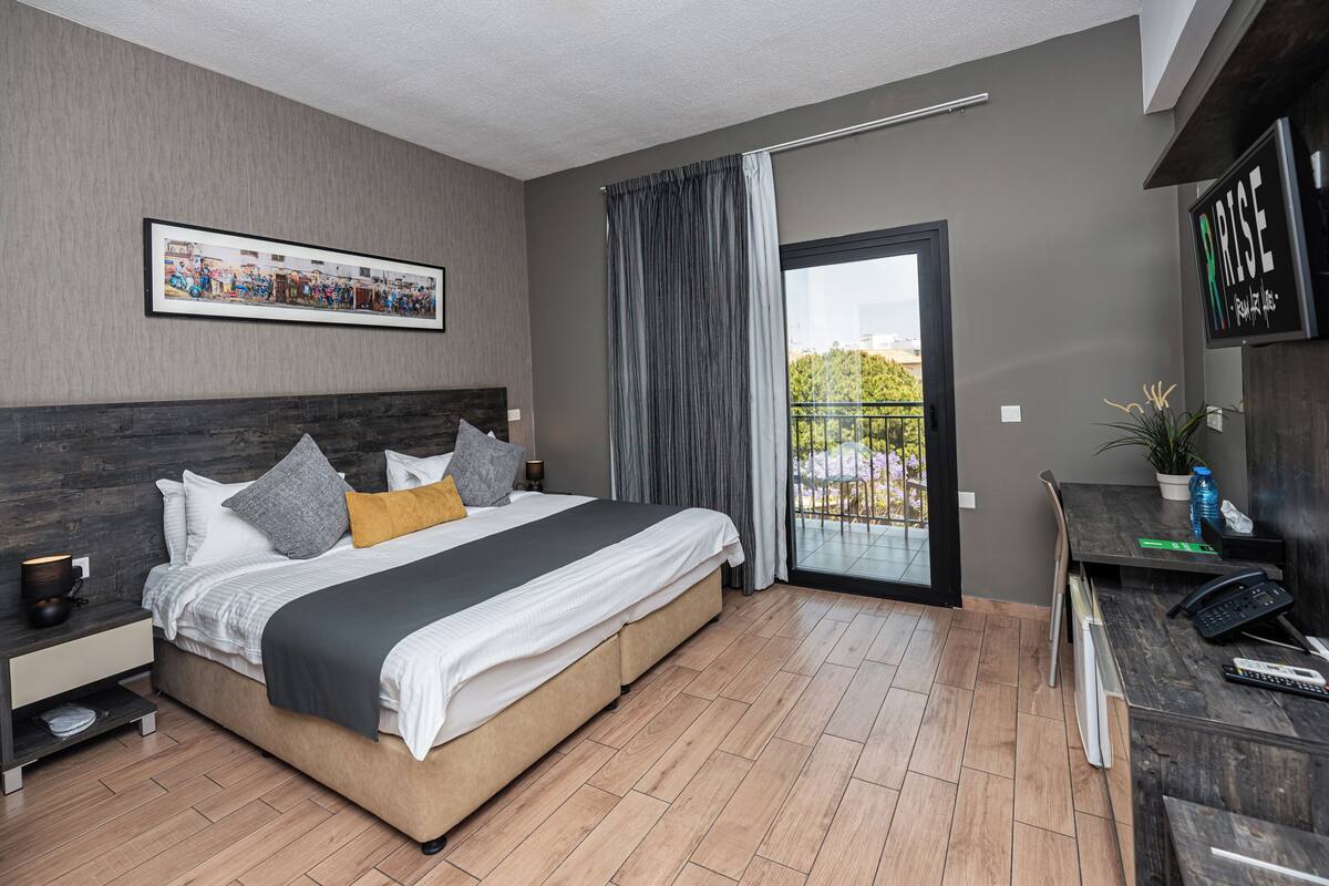 Een moderne hotelkamer met een groot bed, een bureau met telefoon, een televisie en een balkon met uitzicht.