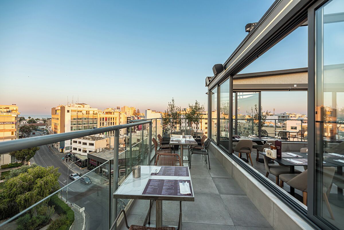 A rooftop terrace with tables and chairs, offering a city view.