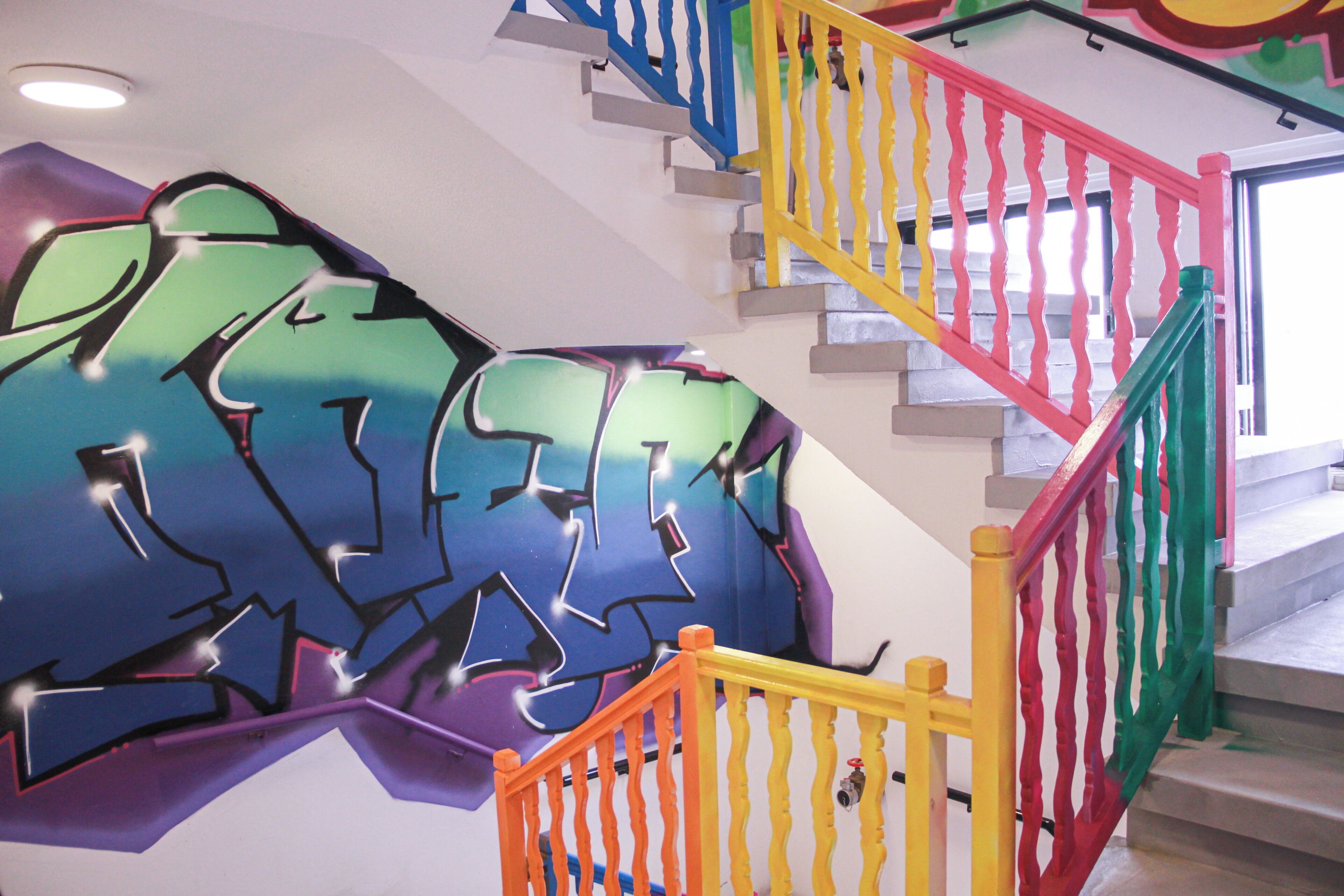 Eine Treppe mit bunten Geländern und einer Wand voller Graffiti.