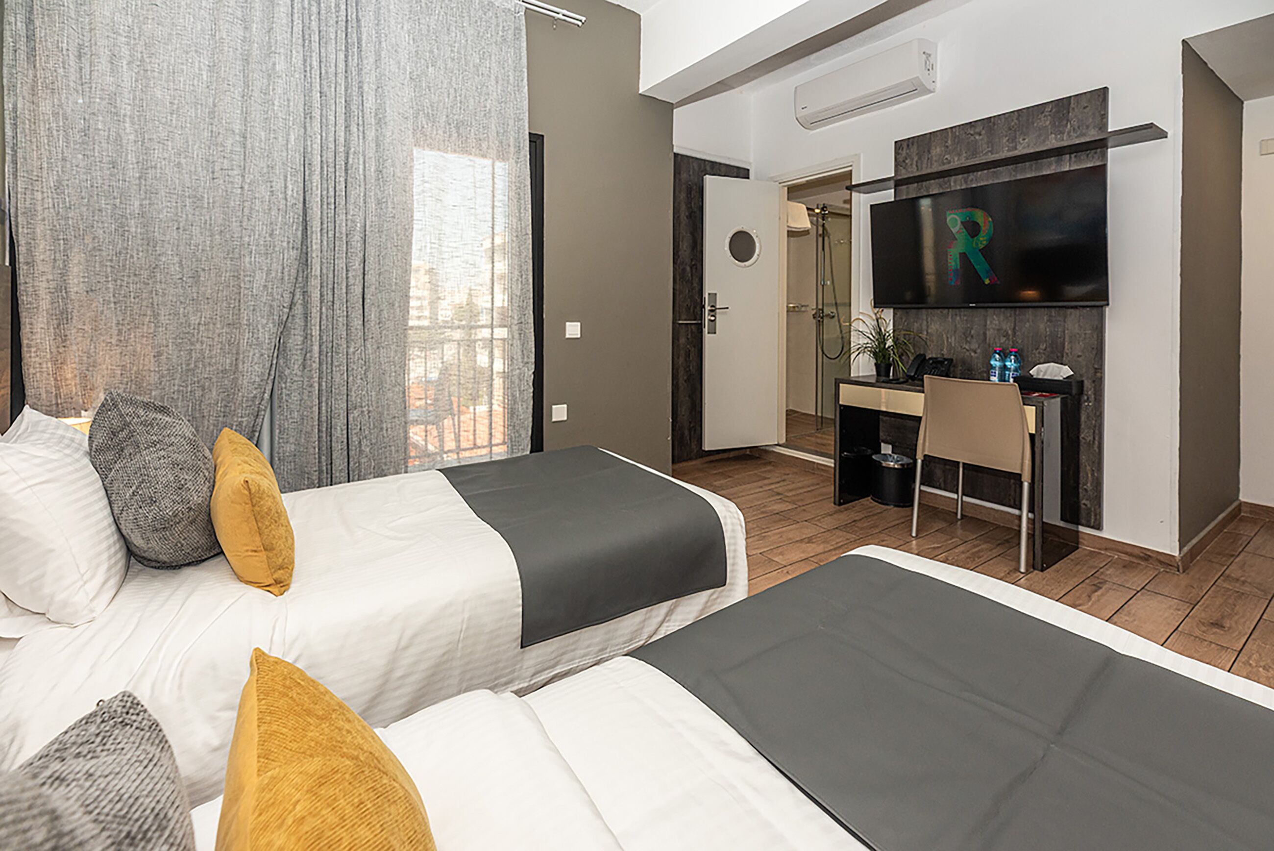 Una habitación de hotel moderna con dos camas, un escritorio, un televisor y una zona de ducha.
