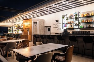 A bar area with a wall-mounted shelf displaying various bottles and a sign that reads 'Don't just walk by, leave a memory behind!'