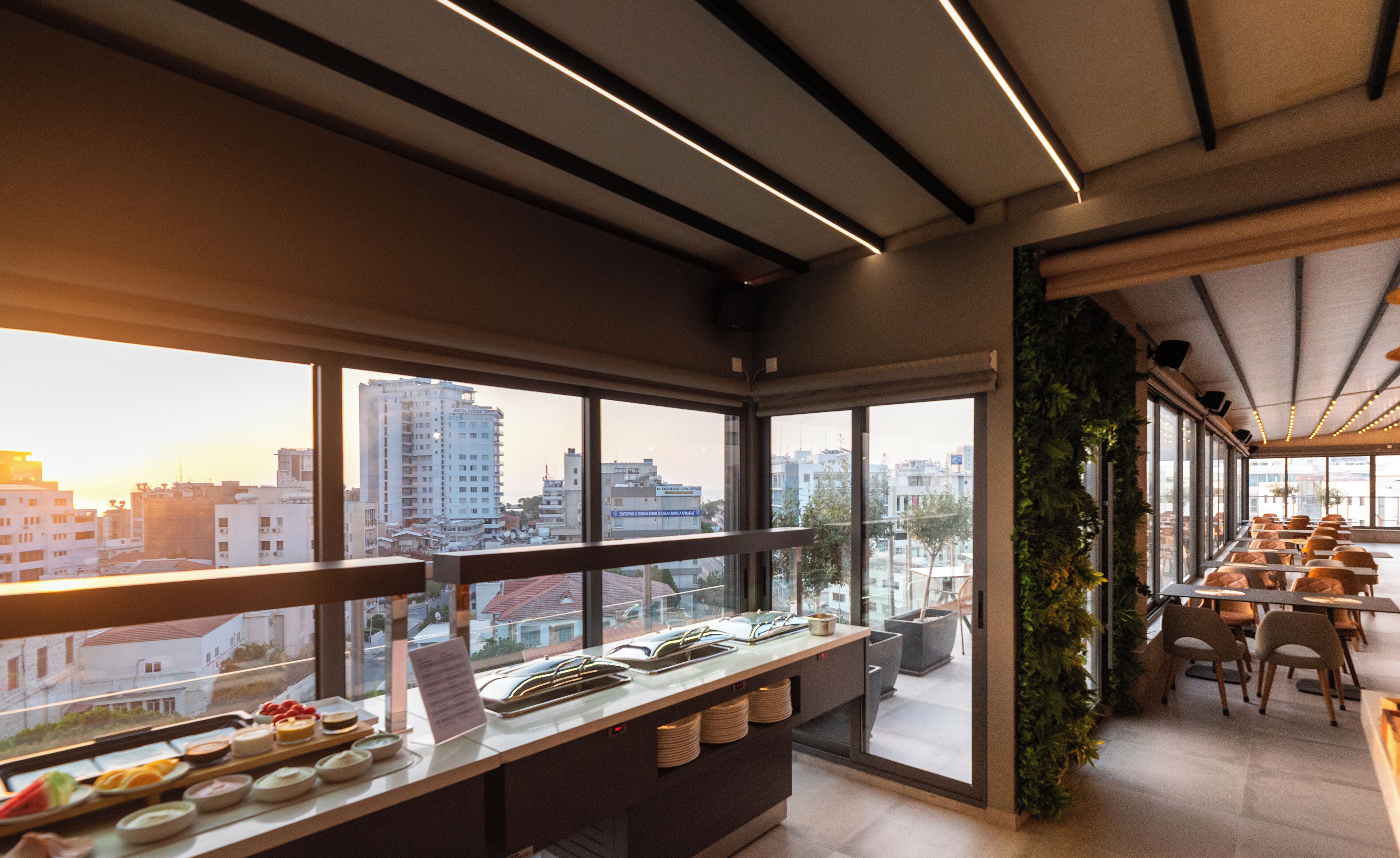 Un restaurante moderno con barra libre, grandes ventanales que ofrecen vistas de la ciudad e iluminación lineal en el techo.