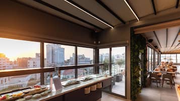 Un restaurante moderno con barra libre, grandes ventanales que ofrecen vistas de la ciudad e iluminación lineal en el techo.