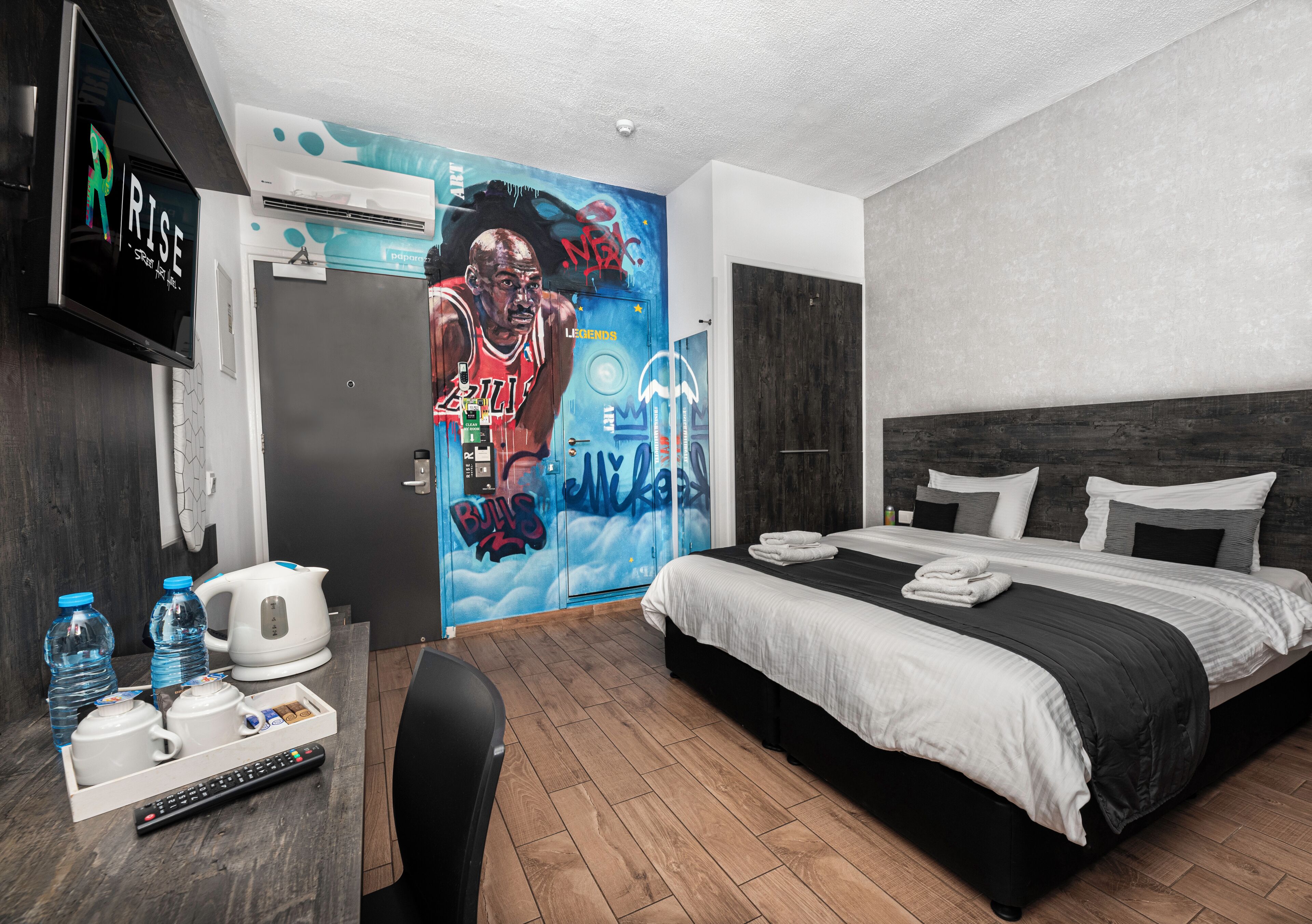 A modern hotel room with a large bed, a flat-screen TV, a coffee maker, and a mural on the wall.