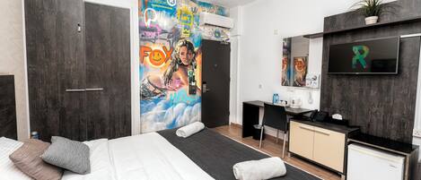A modern hotel room with a large bed, a desk, a small fridge, and a TV mounted on the wall.