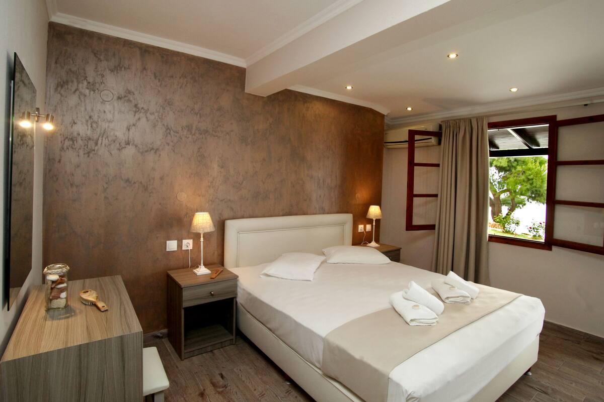 A hotel room with a large bed, two bedside tables with lamps, a mirror, and a window with curtains.