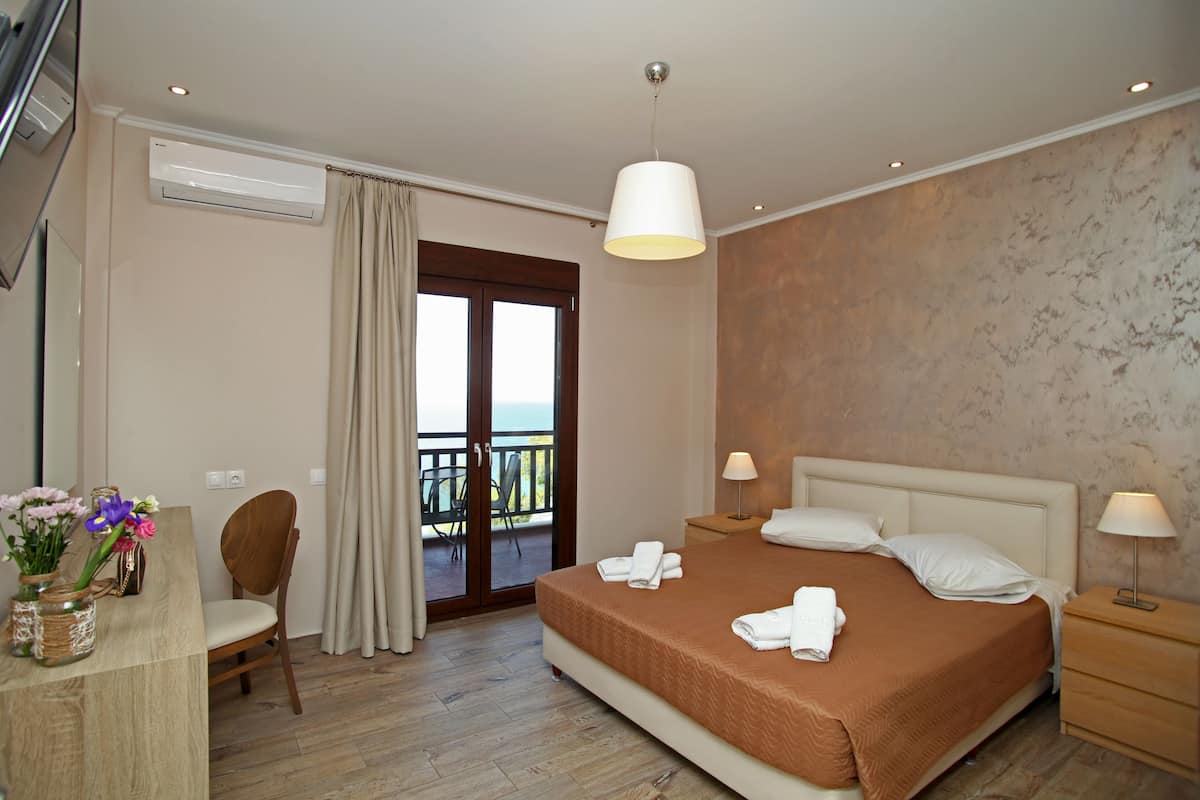 A hotel room with a bed, bedside lamps, a chair, a desk with a vase of flowers, and a balcony with a view.