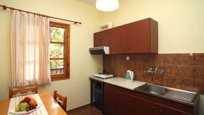 A kitchen with a wooden table, chairs, a sink, cabinets, and a window with curtains. - Apollo Apartments & Studios (Kassandra)