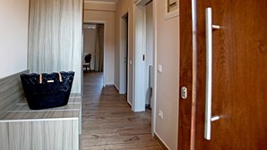 A hallway with a wooden floor, a dark blue woven basket on a bench, and a wooden door with a metal handle. - Apollo Apartments & Studios (Kassandra)
