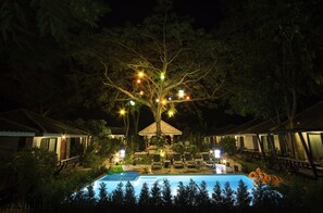 A nighttime view of a resort with a swimming pool, lounge chairs, and a tree decorated with lights. - The Sylvana Pai Boutique Resort (Pai)