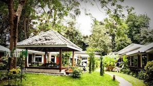 Een hotel in bungalowstijl met een overdekte veranda, omgeven door weelderige begroeiing en palmbomen.