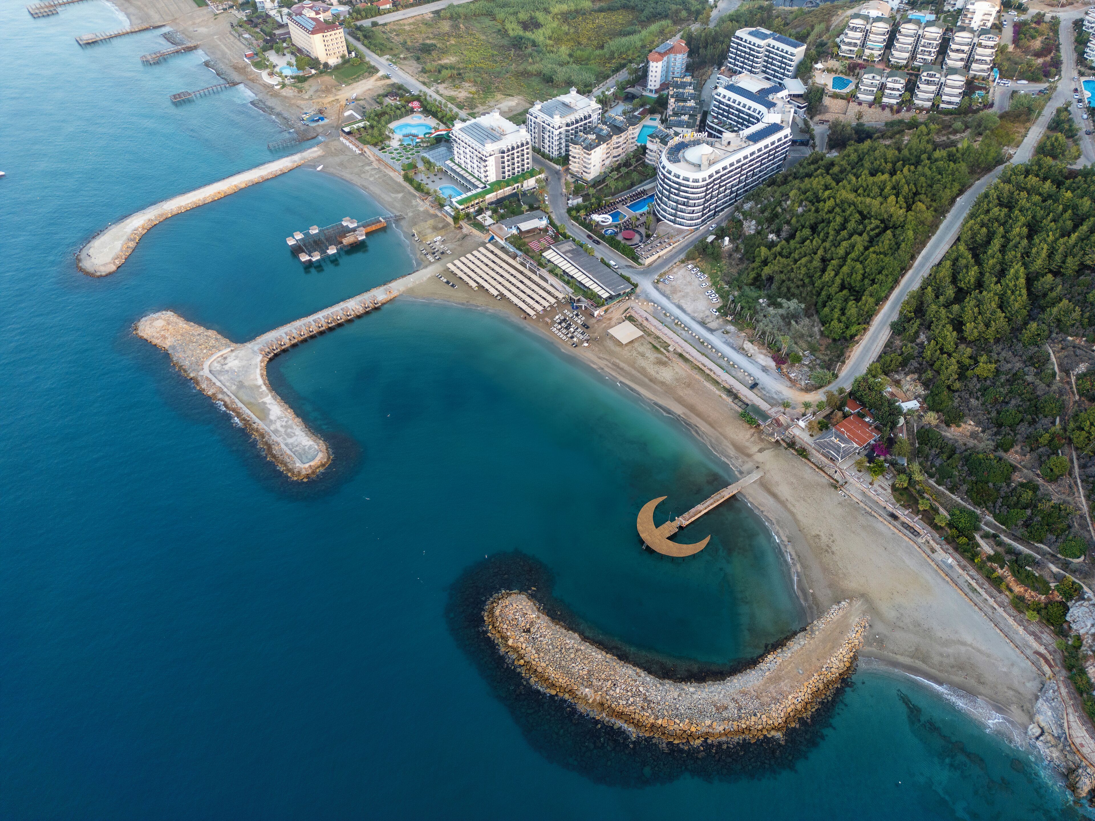 An aerial view of a coastal area with a large marina, multiple high-rise buildings, and a curved breakwater structure.