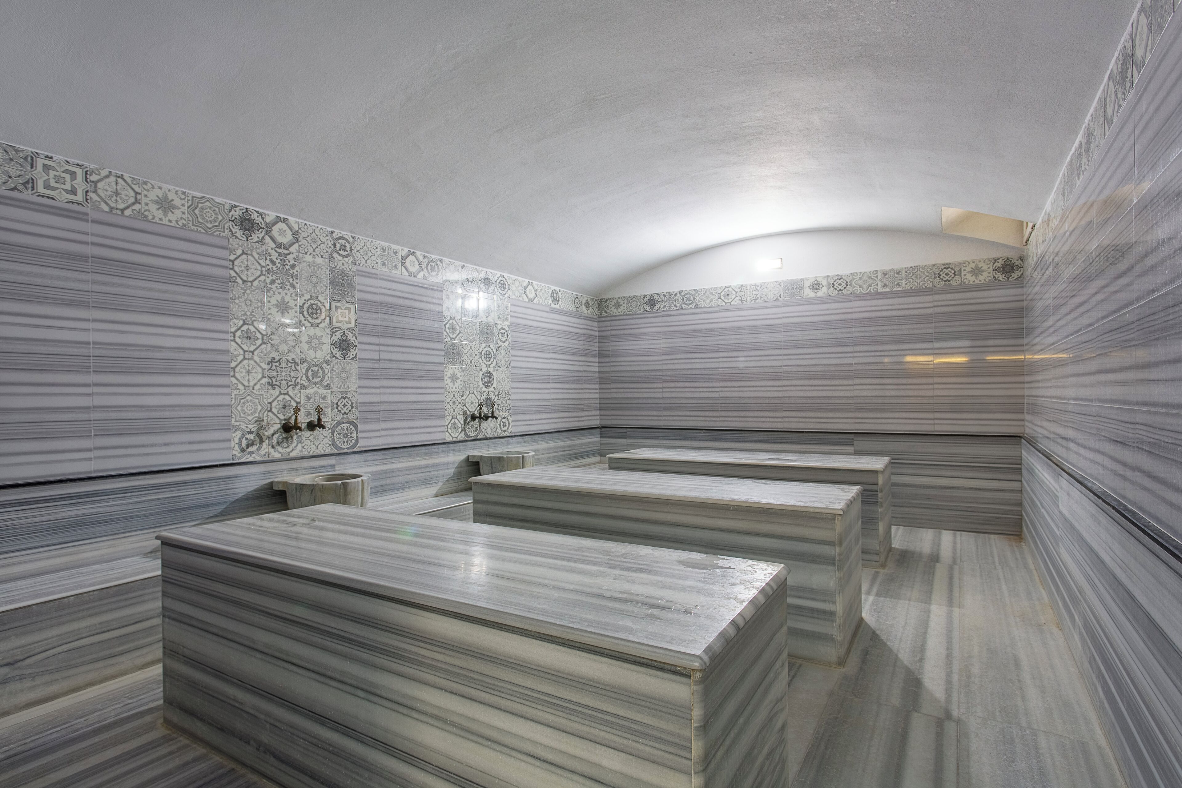 A spa room with marble flooring and walls, featuring a central seating area with benches and a small table.