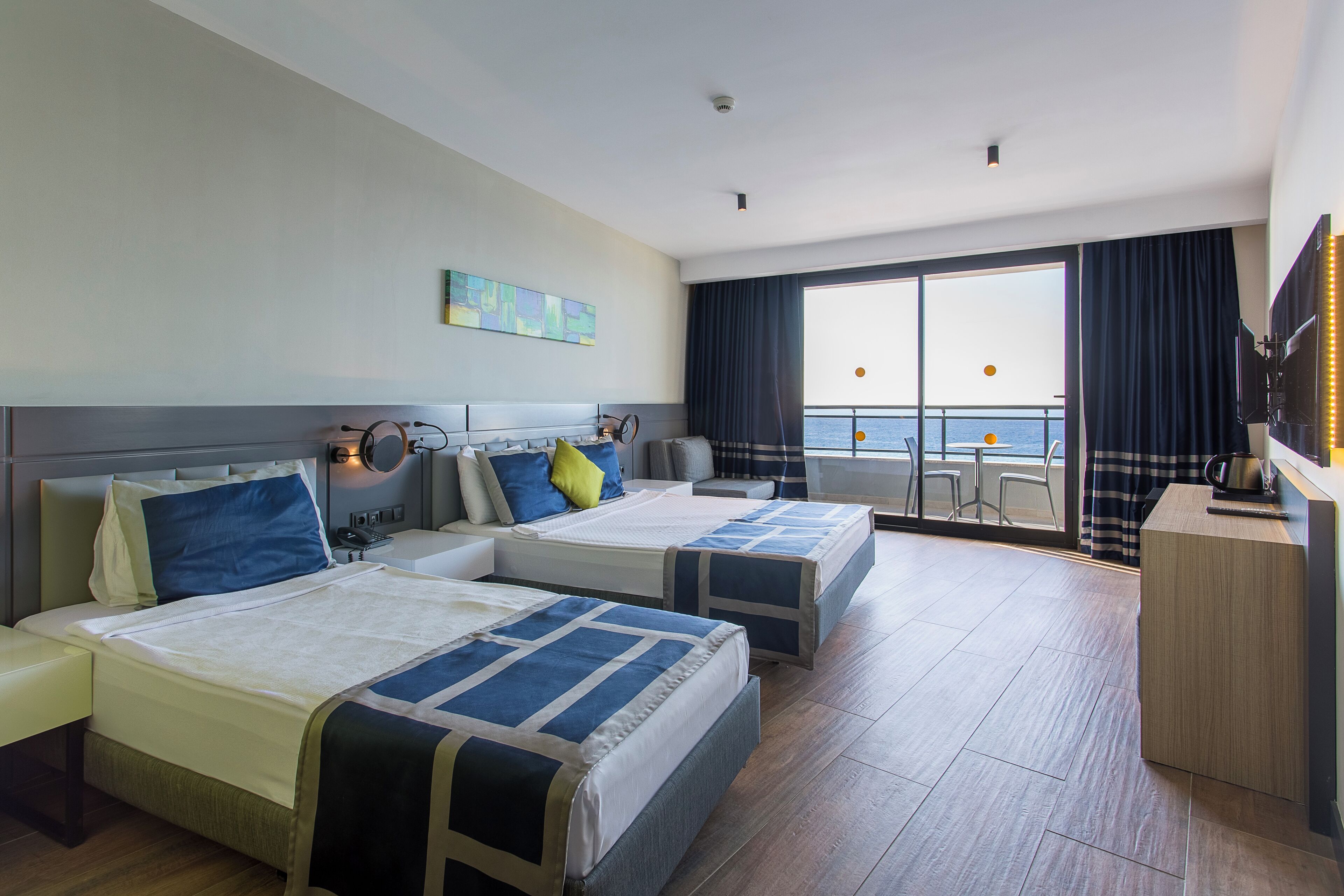 Habitación de hotel con dos camas, un escritorio y un amplio ventanal con vistas al mar.