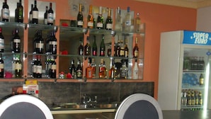 Eine Bar mit Regalen voller Spirituosenflaschen, einem mit "SUPER EURO" beschrifteten Kühlschrank und zwei Barhocker.